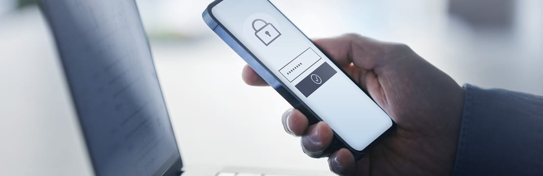 Hand holding a smartphone with a lock icon beside a laptop, illustrating cybersecurity and secure authentication.
